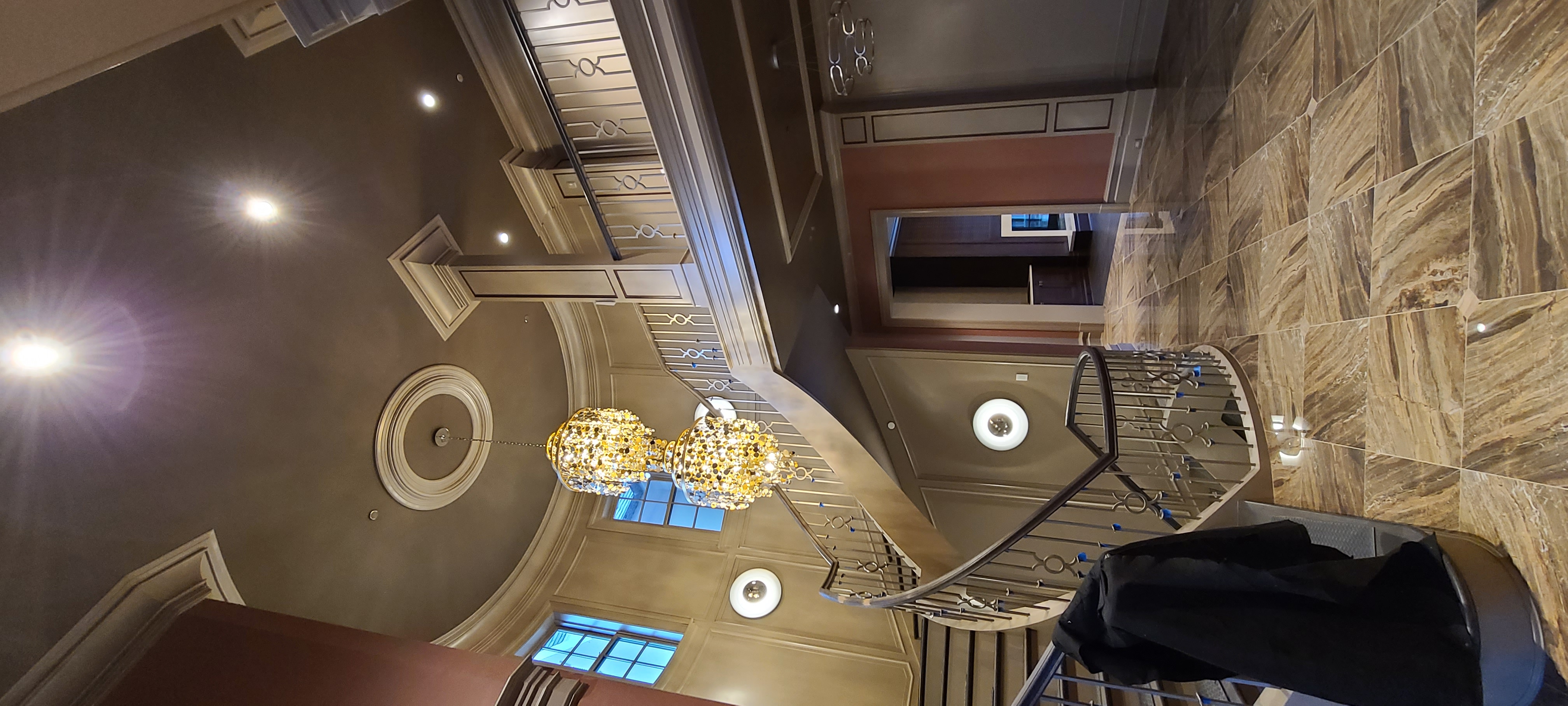 A grand stair landing with chandeliers, ornamental wall mouldings and decorative ceiling treatment