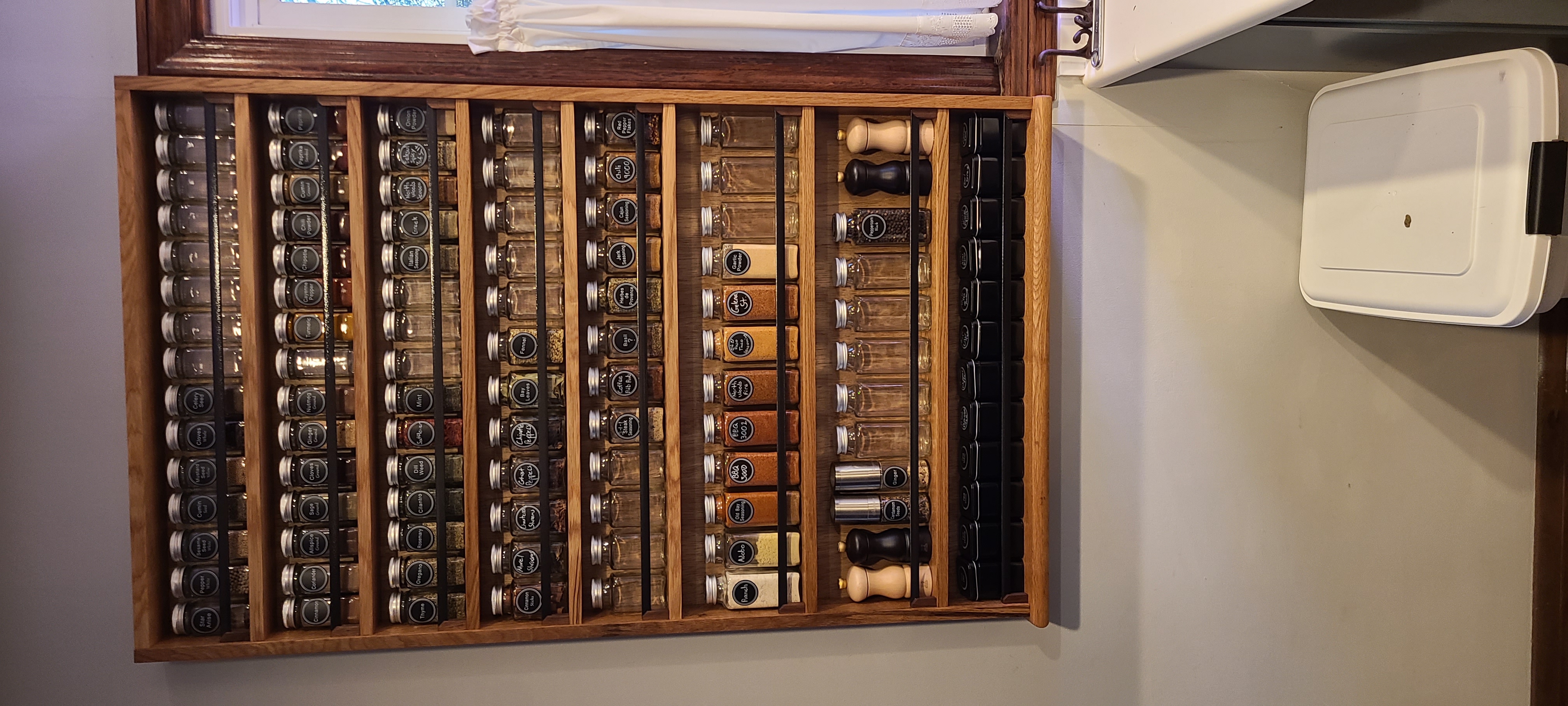 A custom wall-mounted spice rack with eight columns of glass jars, oak frame