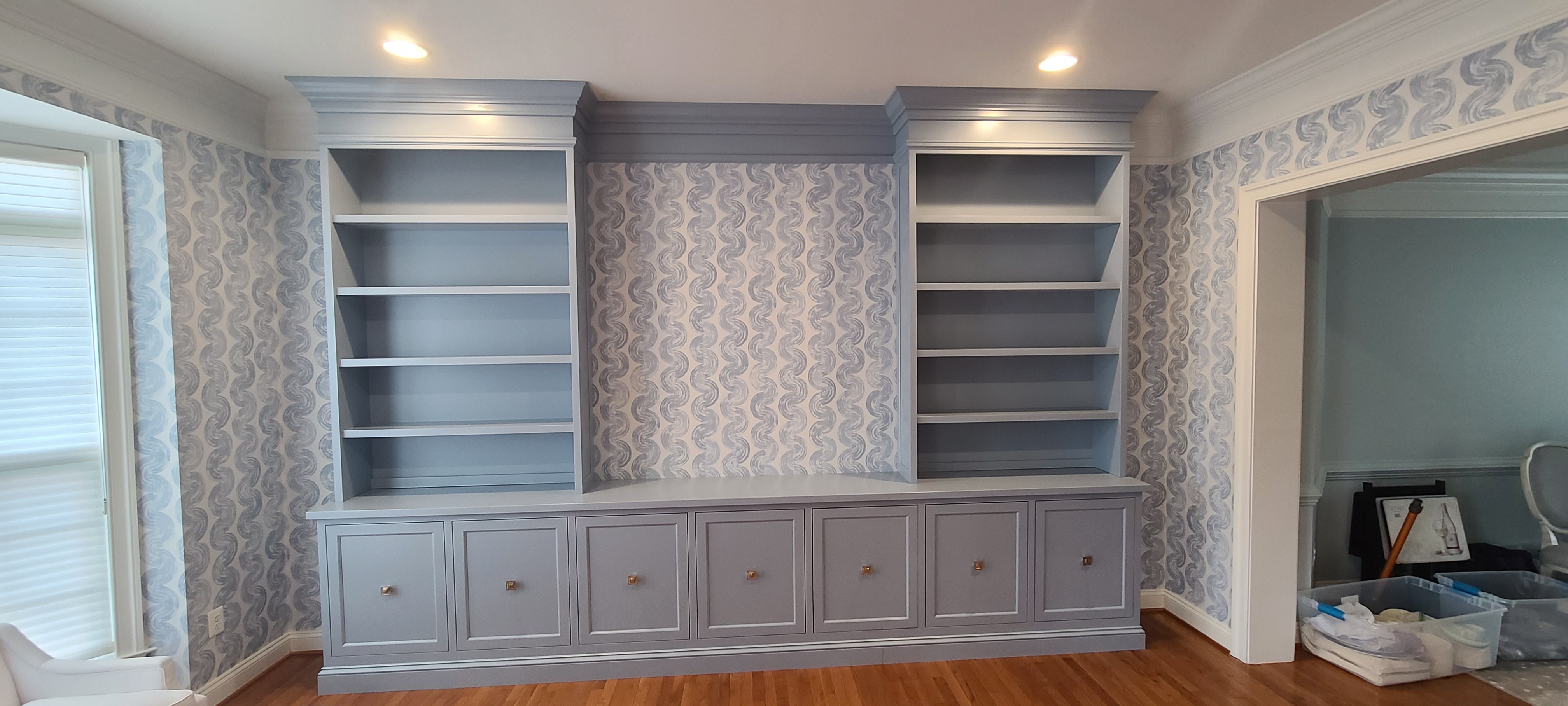 Twin painted bookcase built-ins flanking a media base, blue-grey cabinetry against patterned wallpaper